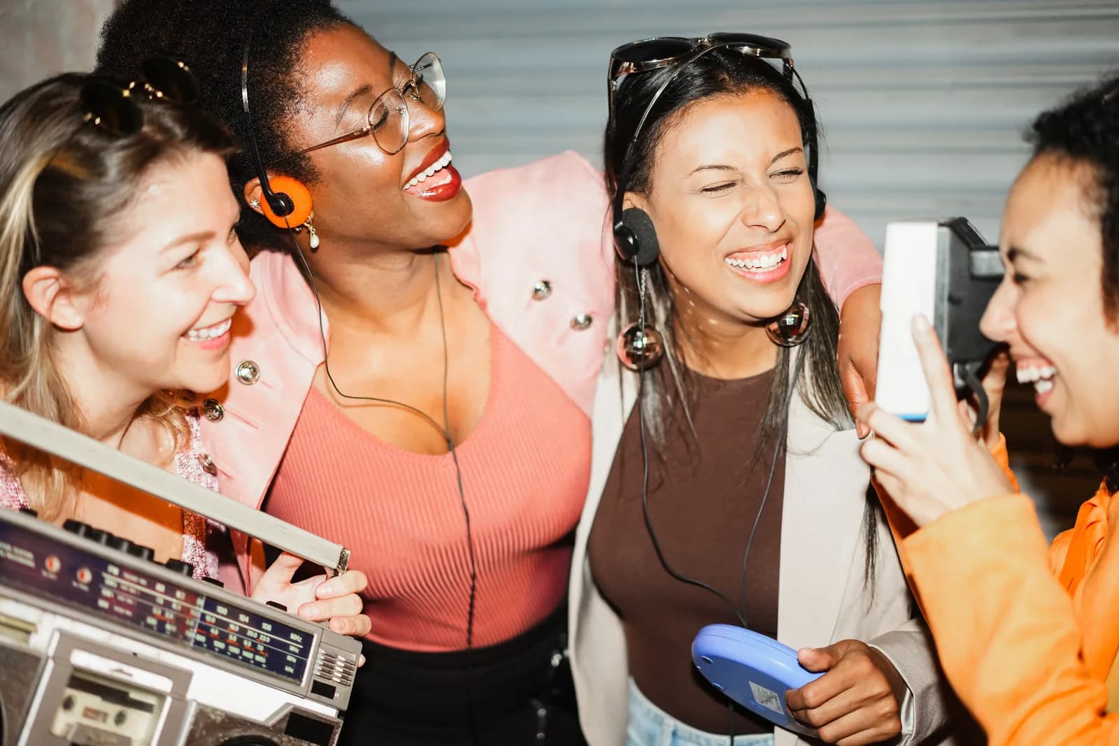 Four friends smiling and listening to music together using headphones and portable music players.